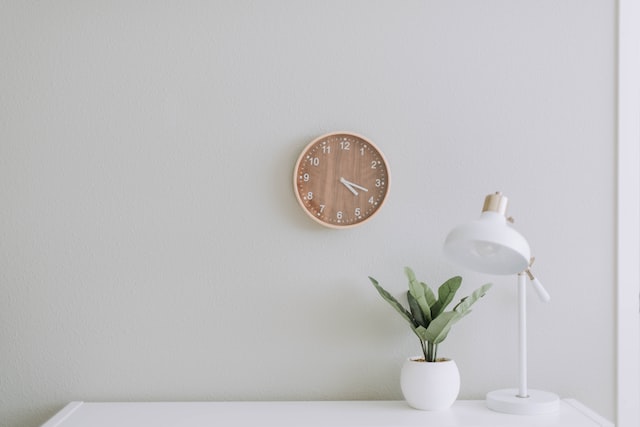 a white table and lamp with a clock on the wall to protect your time and reduce stress and anxiety