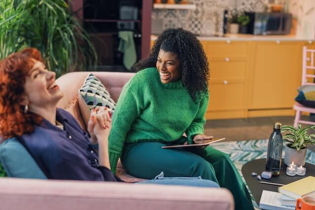 Two young adult women sitting down, laughing and sharing tips on making friends with social anxiety