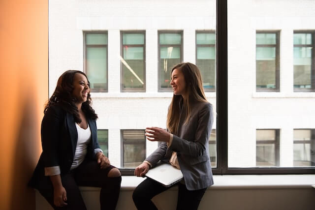 Two young working women sitting down talking about ways to stop procrastinating