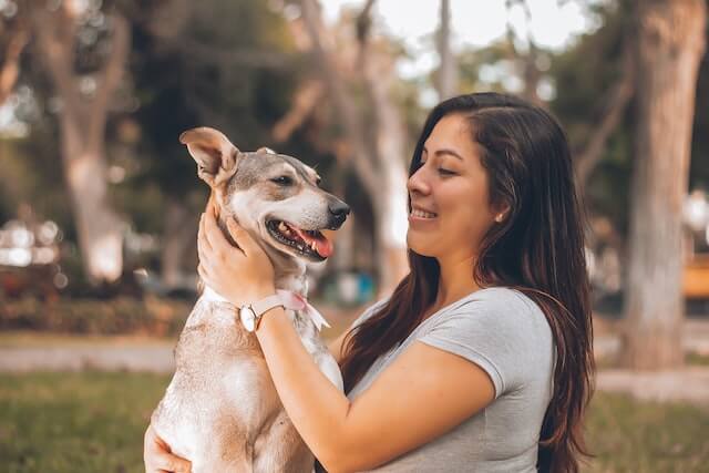 a young adult woman smiling using her hands to touch her pet dog