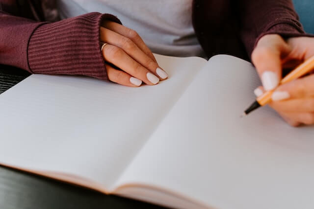 A young adult woman sitting down with an open notebook and a pen