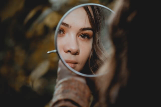 Young adult woman looking at her reflection in a mirror as an example of toxic self-criticism. 