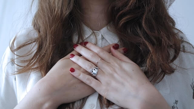 A young adult woman with hands crossed over her chest. Practicing self-compassion to understand where self-criticism comes from.