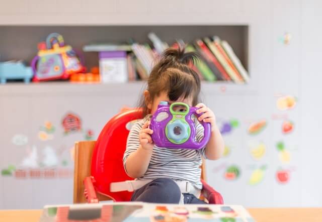 Young toddler girl holding a toy camera. Reflects anxious habits 