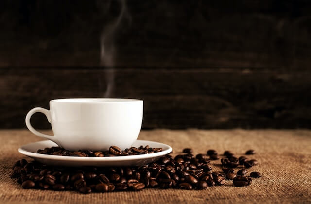 Cup of hot coffee with steam and coffee beans on the table. 