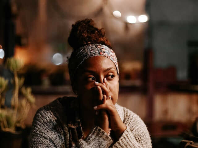 young adult woman of color with hands on her face may be thinking how to get out from negative thoughts