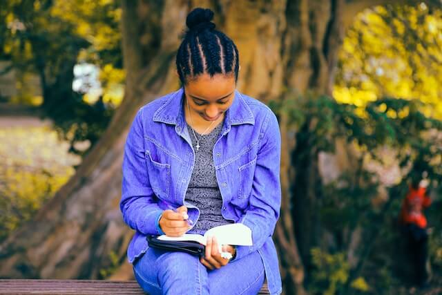 Young adult woman sitting down and writing in a journal as a way to get rid of negative automatic thoughts